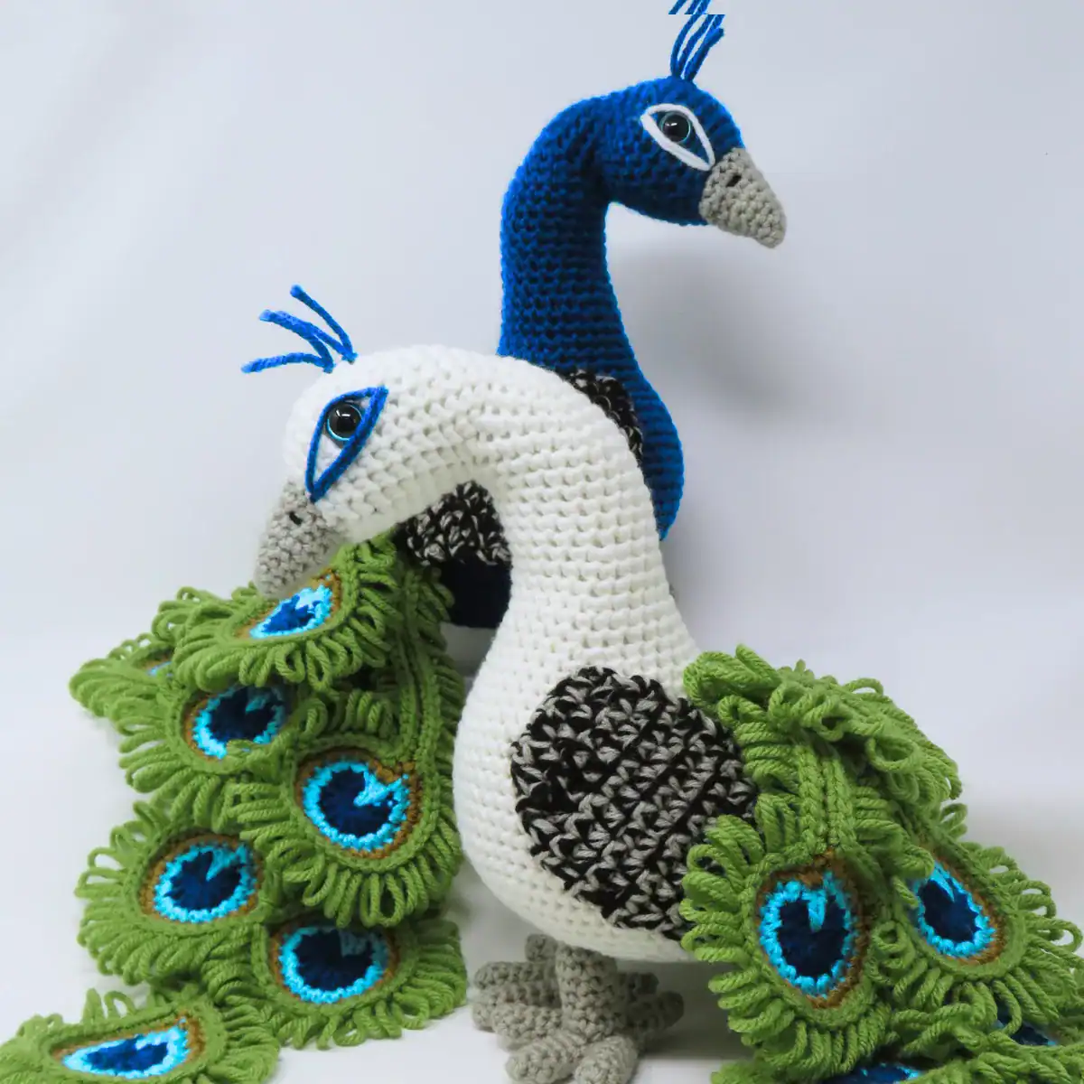 Realistic crochet peacocks, one white and one blue, loop stitch feathers out behind them