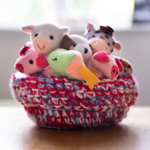 crochet basket made with scrap yarn in red, blue and white, holding lots of small stuffed animals