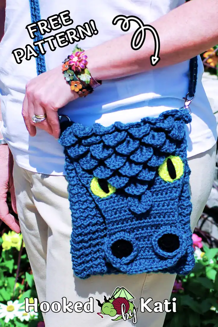 A teal crochet dragon face purse with yellow eyes